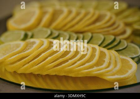 Un arrangement visuellement attrayant de fines tranches de citrons et de citrons verts affichés en rangées se chevauchant sur une plaque de verre, mettant en valeur des teintes d'agrumes vives et de F. Banque D'Images
