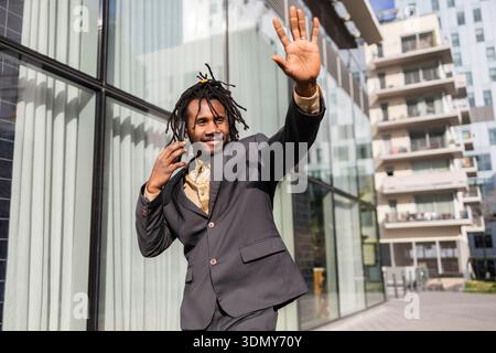 Homme d'affaires afro-américain avec des dreadlocks posant en toute confiance à l'extérieur dans un cadre urbain. Il porte un costume noir élégant, exsudant un sens de p Banque D'Images