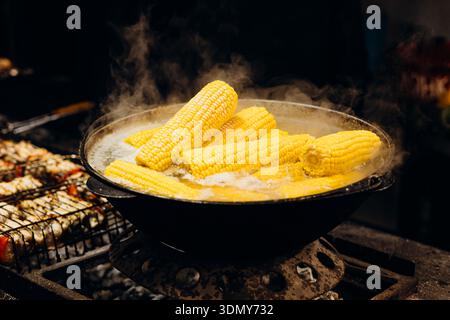 Maïs frais sur l'épi bouillant dans une grande casserole à un marché alimentaire de rue animé. La vapeur monte pour créer une atmosphère accueillante, capturant l'essence de Banque D'Images