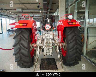 Un tracteur agricole rouge doté de pneus arrière larges est bien en vue à l'intérieur, mettant en valeur ses machines dans un environnement industriel moderne Banque D'Images