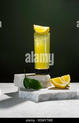 Un grand verre de thé glacé au citron frais est placé sur un fond sombre, garni d'un coin de citron. La boisson repose sur des dalles de marbre, avec du citron frais Banque D'Images