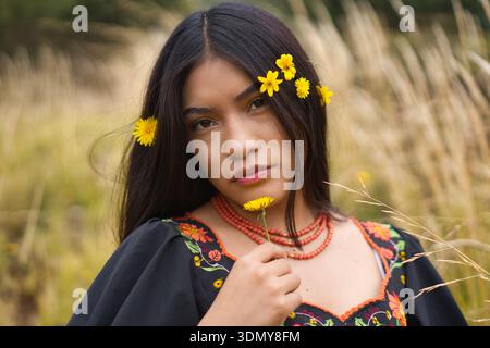 Mannequin indigène portant une robe brodée noire et un collier pose dans un champ de hautes herbes avec de petites fleurs jaunes ornant son long d Banque D'Images