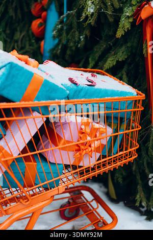 Un panier orange vif rempli de cadeaux magnifiquement emballés et de rubans colorés, sur fond festif avec la neige légèrement poussiéreuse Banque D'Images
