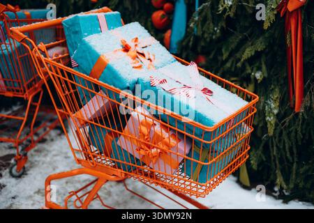 Un panier orange est rempli de cadeaux magnifiquement emballés, ornés de rubans vibrants, placés à l'extérieur avec des décorations festives environnantes et Banque D'Images