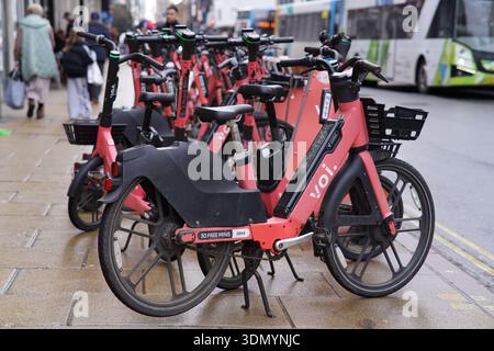 Rangée de scooters électriques VOI rouges garés sur un trottoir du centre-ville de Cambridge près d'un bus. Cambridge, Angleterre Banque D'Images