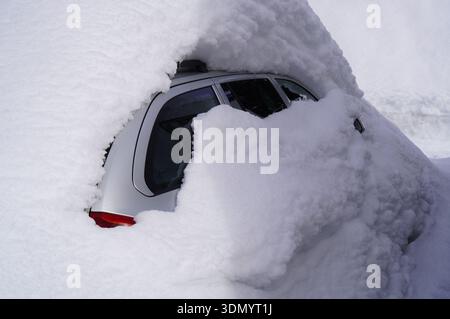 Voiture argentée enterrée sous une épaisse couche de neige fraîche. Une forte chute de neige a presque complètement recouvert un véhicule stationné. Banque D'Images