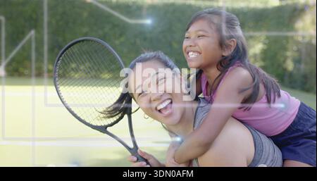 Donnant femme adulte portant l'enfant piggyback sur court de tennis, tenant la raquette de tennis, dans le réservoir gris Banque D'Images