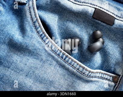 Écouteurs sans fil placés dans la poche avant du Jean denim, représentant la technologie audio moderne et le style de vie décontracté Banque D'Images