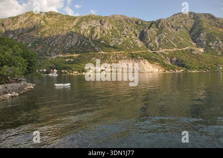 Une scène côtière sereine présente de l'eau calme reflétant les montagnes majestueuses et la végétation luxuriante. Les bateaux reposent doucement sur la surface lorsque le soleil s'illumine Banque D'Images
