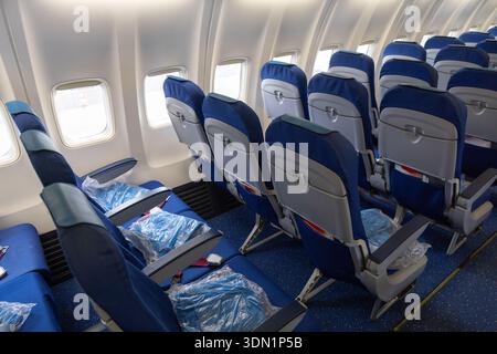 Rangée de sièges économiques bleus à l'intérieur d'un jet passager moderne avec vitres, accoudoirs et ceintures de sécurité lumineux visibles. Cabine vide propre pour le voyage, l'aviation et le marketing aérien Banque D'Images