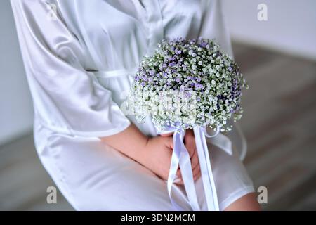 Mariée assise sur la chaise tenant bouquet de mariage Banque D'Images