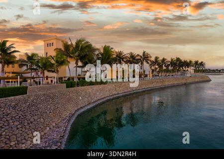 Vue aérienne spectaculaire de Hawana Salalah à Oman au coucher du soleil. L'image capture les bâtiments de la station et les palmiers luxuriants bordant une voie navigable courbe, avec t Banque D'Images