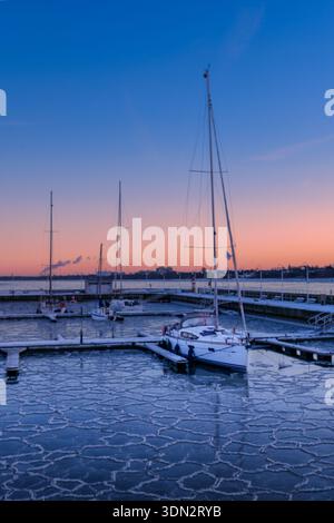 Une scène hivernale pittoresque avec plusieurs voiliers amarrés dans une marina à Sopot, en Pologne, au coucher du soleil. L'eau est partiellement gelée avec PA complexe Banque D'Images
