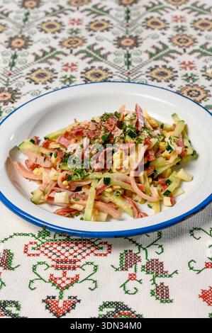Salade de viande avec jambon, saucisse, concombre frais et oeuf saupoudré d'herbes. Salade maison avec jambon et concombre frais dans une assiette légère sur la table Banque D'Images