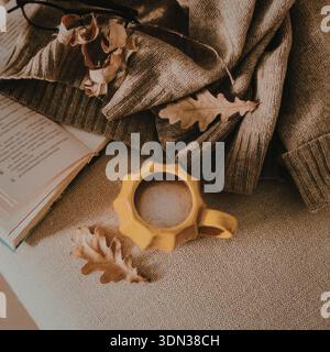 Une scène automnale sereine avec une tasse, un livre et un pull sur une surface confortable. Banque D'Images