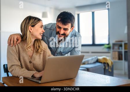 Heureux jeune diversifié, couple multiethnique budget de planification, lecture de bonnes nouvelles sur ordinateur portable à la maison Banque D'Images
