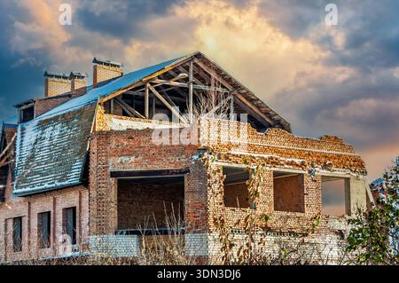 Un bâtiment en briques partiellement détruit avec des dommages structurels visibles se dresse contre un ciel dramatique, suggérant une résilience et une décomposition. Banque D'Images