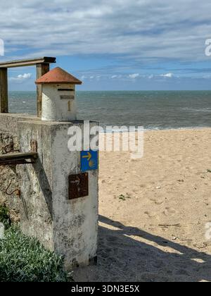 Esteiro Beach, Portugal - 24 mars 2025 : Camino de Santiago waymark côtier avec coquille jaune et flèche sur pilier en béton près de la plage de sable, Atlantique Banque D'Images