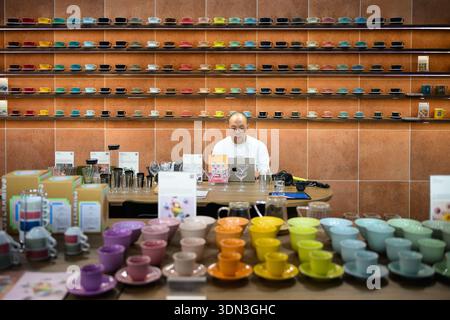 Un exposant travaillant sur un ordinateur portable entouré de tasses à café colorées à Host Milano 2025. Culture du café et des affaires au salon de l'hospitalité de Milan. Banque D'Images