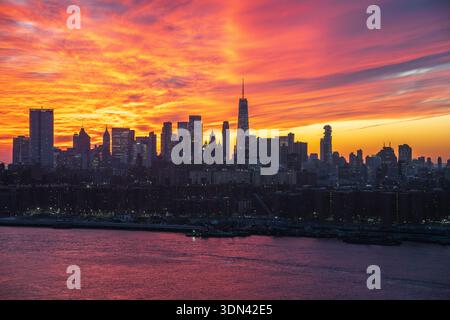 La vue d'un lever de soleil ardent peint l'horizon de New York dans des teintes vibrantes d'orange et de rose, reflétées dans les eaux tranquilles ci-dessous, New York, New York, ONU Banque D'Images