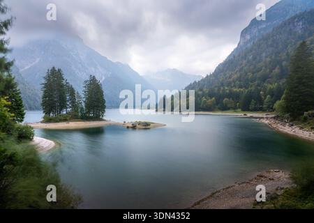 Vue aérienne des eaux tranquilles reflétant le ciel couvant, encadrée par l'étreinte accidentée des Alpes juliennes et des forêts luxuriantes, du Trentin, du Frioul-Vénétie Banque D'Images
