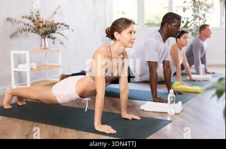 Multinationales hommes et femmes yoga montrant la pose de planche dans le centre de bien-être Banque D'Images