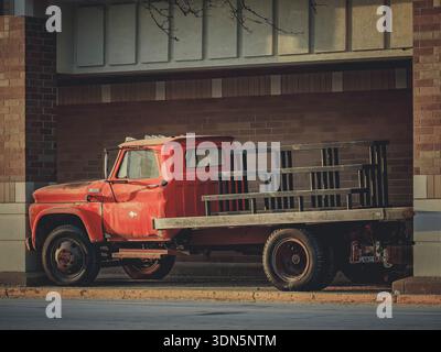 Camion à plateau Chevrolet C60 rouge vintage avec peinture altérée garé à côté d'un bâtiment en briques, illuminé par la lumière chaude du soleil du soir dans l'Illinois. Banque D'Images