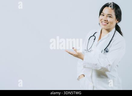 Médecin féminin asiatique souriant montrant un espace vide isolé. Jeune médecin asiatique présentant quelque chose d'isolé Banque D'Images