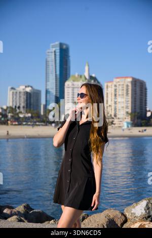 Femme en robe noire près de l'eau avec des gratte-ciel derrière Banque D'Images