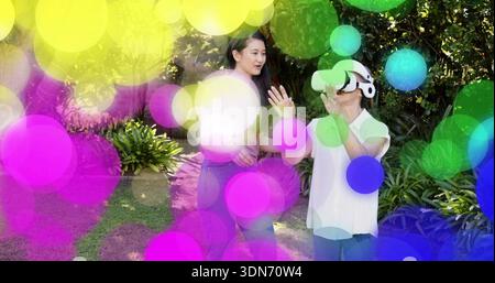Guide femme senior portant casque VR par femme mi-adulte dans le jardin, avec bokeh coloré Banque D'Images