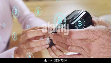 Couple senior portant des manches longues tenant un portefeuille crypto noir sur la table à la maison, superpositions Bitcoin Banque D'Images