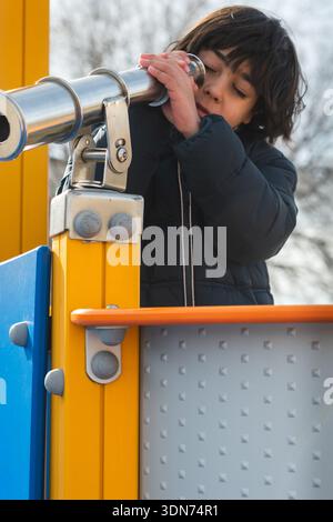 Enfant regardant à travers un télescope sur une aire de jeux, favorisant la curiosité et l'exploration Banque D'Images