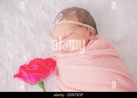 Bébé nouveau-né endormi dans une enveloppe rose avec une fleur de rose sur fond de fourrure blanche. Banque D'Images