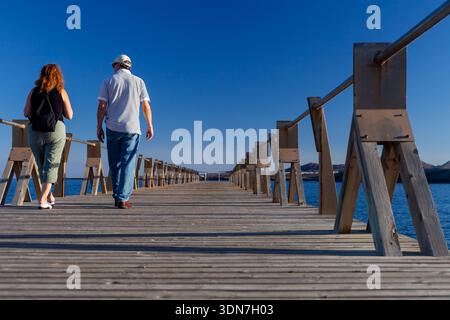Couple senior marchant le long d'une jetée en bois à Sunset on the Beach Banque D'Images