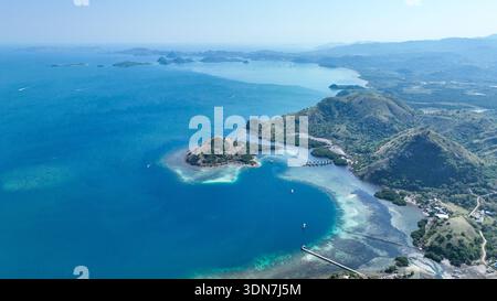 Panoramique aérien de Labuan Bajo et du parc national de Komodo, où les collines émeraude se fondent en baies bleu foncé parsemées d'îles et de bateaux. Un gatewa tranquille Banque D'Images