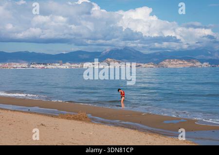 Alicante, Espagne- 13 janvier 2026 : jeune femme sur le rivage sur la plage en hiver à Arenales del sol, Alicante, sud de l'Espagne Banque D'Images