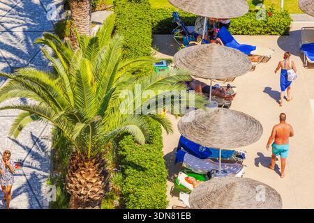 Vue de dessus de touristes se relaxant sous des parasols près de la piscine avec un palmier en arrière-plan. Grèce. Rhodes. Banque D'Images