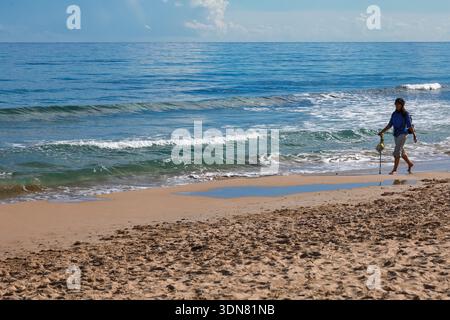 Alicante, Espagne- 13 janvier 2026 : jeune femme marchant sur le rivage sur la plage en hiver à Arenales del sol, Alicante, dans le sud de l'Espagne Banque D'Images