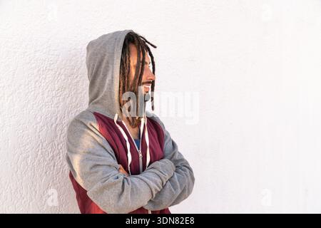 Jeune homme avec des dreadlocks et un sweat à capuche de profil, debout devant un mur blanc Banque D'Images