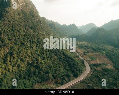 Une route sinueuse traverse des montagnes verdoyantes sous un ciel nuageux, créant une vue panoramique. Baie de LAN Ha, Cat Ba, Vietnam Banque D'Images