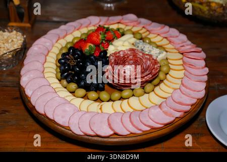 Planche de charcuterie sophistiquée avec charcuterie, fromages assortis, fruits frais et olives sur plateau en bois. Parfait pour les photos gourmandes, les événements et foo Banque D'Images