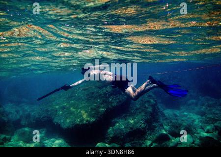 Un freeplongeur portant des palmes nage avec un speargun au-dessus d'un fond rocheux dans la mer Méditerranée, Mellieha, région du Nord, Malte, 17 octobre, 2025. le Banque D'Images