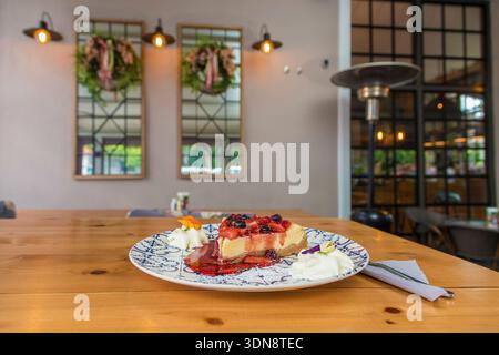 Délicieuse tranche de cheesecake crémeux garnie d'une sauce aux fruits de la forêt vibrante, servie sur une assiette décorative en céramique avec des poupées de crème fouettée, se Banque D'Images