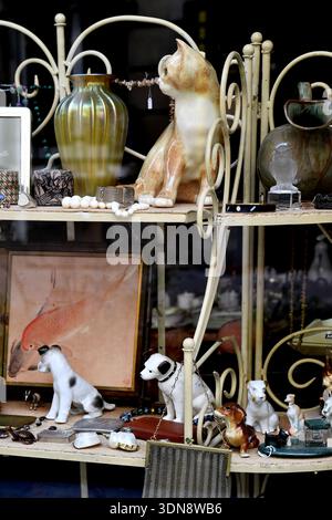 une étagère en métal blanc à l'intérieur d'une vitrine de magasin d'antiquités, remplie de divers objets décoratifs vintage, vitrine dans une rue du 9e arrondissement de Paris - France Banque D'Images
