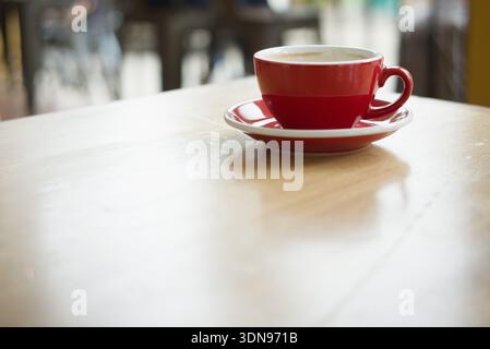 Une tasse à café en céramique rouge éclatante et une soucoupe reposent sur une table de café en bois de couleur claire. L'image présente une faible profondeur de champ avec un b magnifiquement Banque D'Images