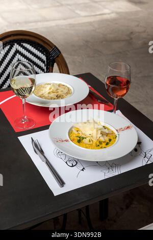 dîner en plein air avec plats de pâtes gastronomiques parfaitement assortis à des verres de vin blanc et rosé frais sur une élégante terrasse ensoleillée. SOF Banque D'Images