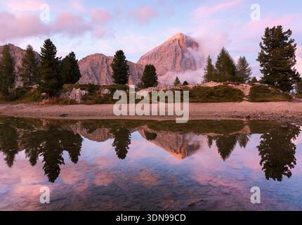 Reflet de montagne sur un lac calme et tranquille dans les Dolomites, souligné par quelques couleurs roses dans le ciel et sur l'eau réfléchissante. Banque D'Images