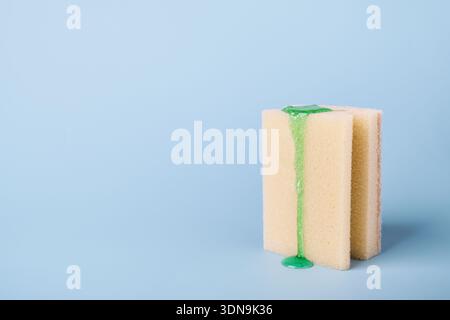 EPONGE de nettoyage avec du détergent vaisselle liquide qui s'égoutte sur fond bleu clair Banque D'Images