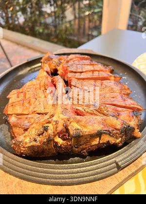 Bifteck grillé en T‑bone coupé en tranches sur une assiette noire rustique Banque D'Images