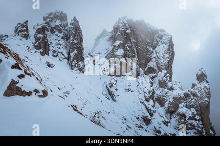 Spectaculaire vue hivernale des flèches Grignetta émergeant d'un épais brouillard et de nuages bas. Paysage alpin Moody avec des sommets rocheux enneigés dans les montagnes Banque D'Images
